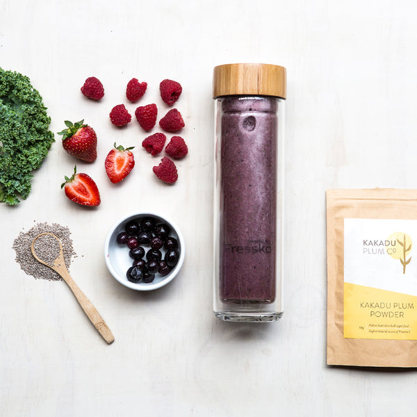 Berry smoothie in glass flask surrounded by kakadu plum powder chia seeds kale and berries