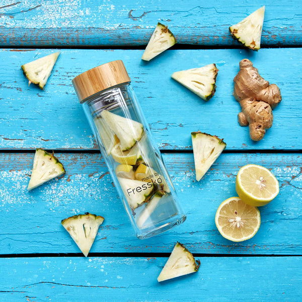 Fruit water in glass fressko flask surrounded by pineapple ginger and lemon